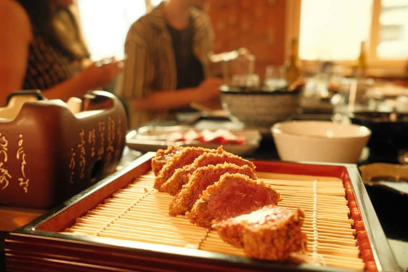 SHOKUDO Izakaya crispy fried items on bamboo mat with tea service and diners in background.